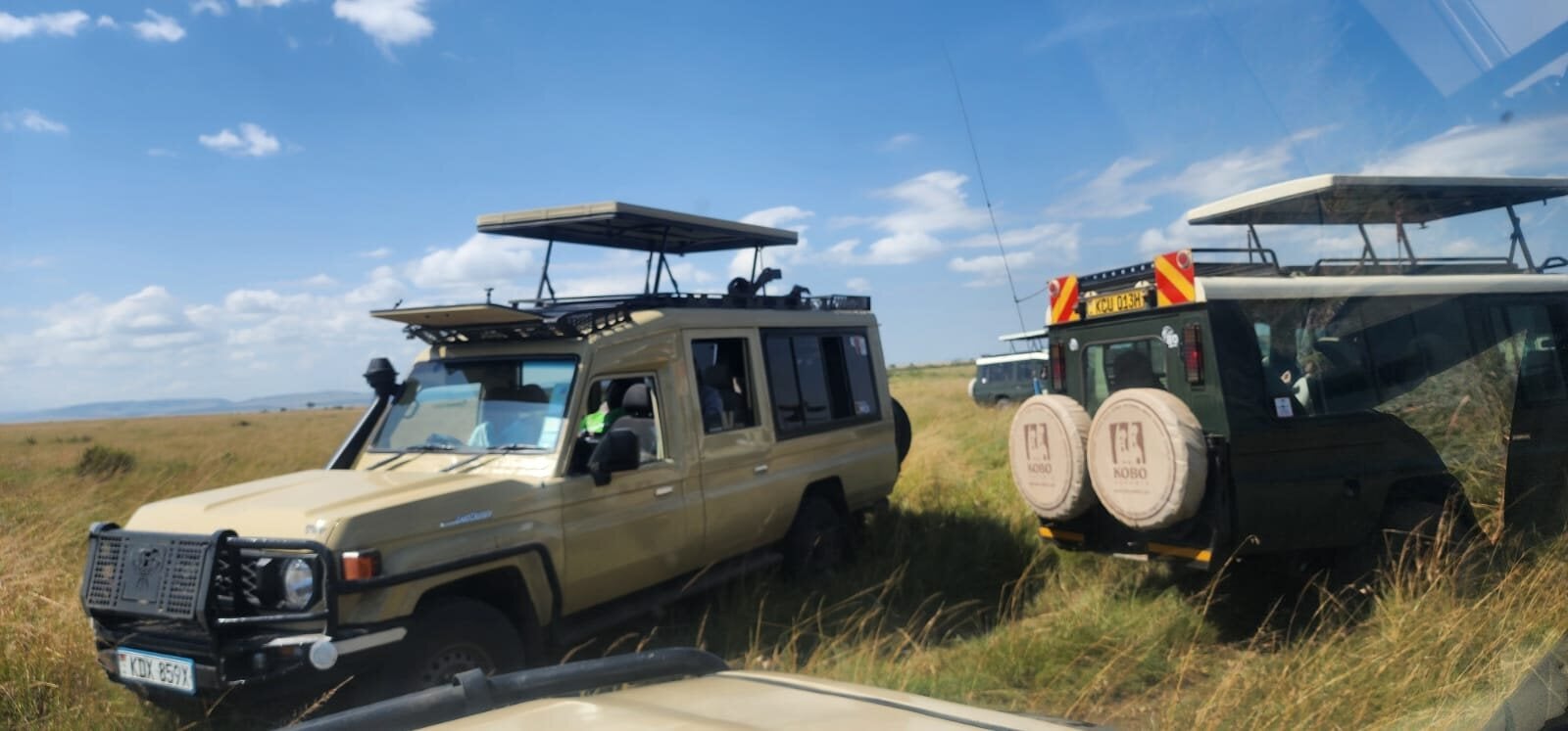 Two neutral-coloured 4x4 safari vehicles on open grassland